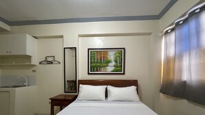A hotel room with a bed, a bedside table, a mirror, a sink, and a painting on the wall. - Lawton Residences powered by Cocotel (Taguig)