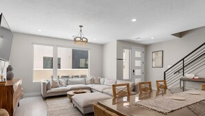A spacious living area with a large sofa, dining table, and a staircase leading to another level. - Bare Feet Retreat by RedAwning (St. George)