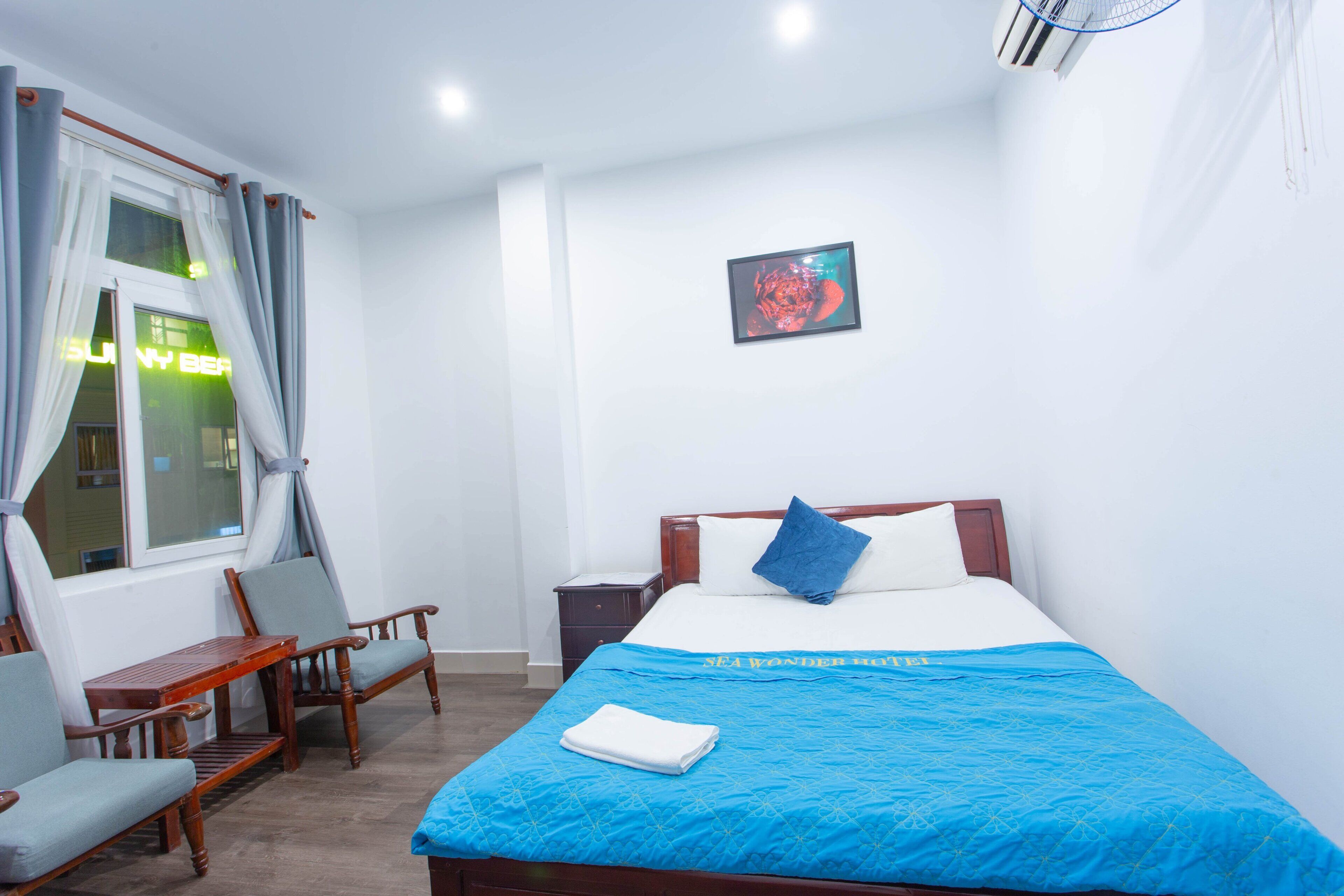 Una camera d'albergo con un letto, una scrivania, due sedie, un comodino e una finestra con tende.