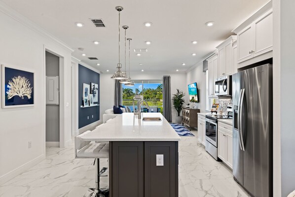 A modern kitchen with a central island, stainless steel appliances, and a view of a lush garden.