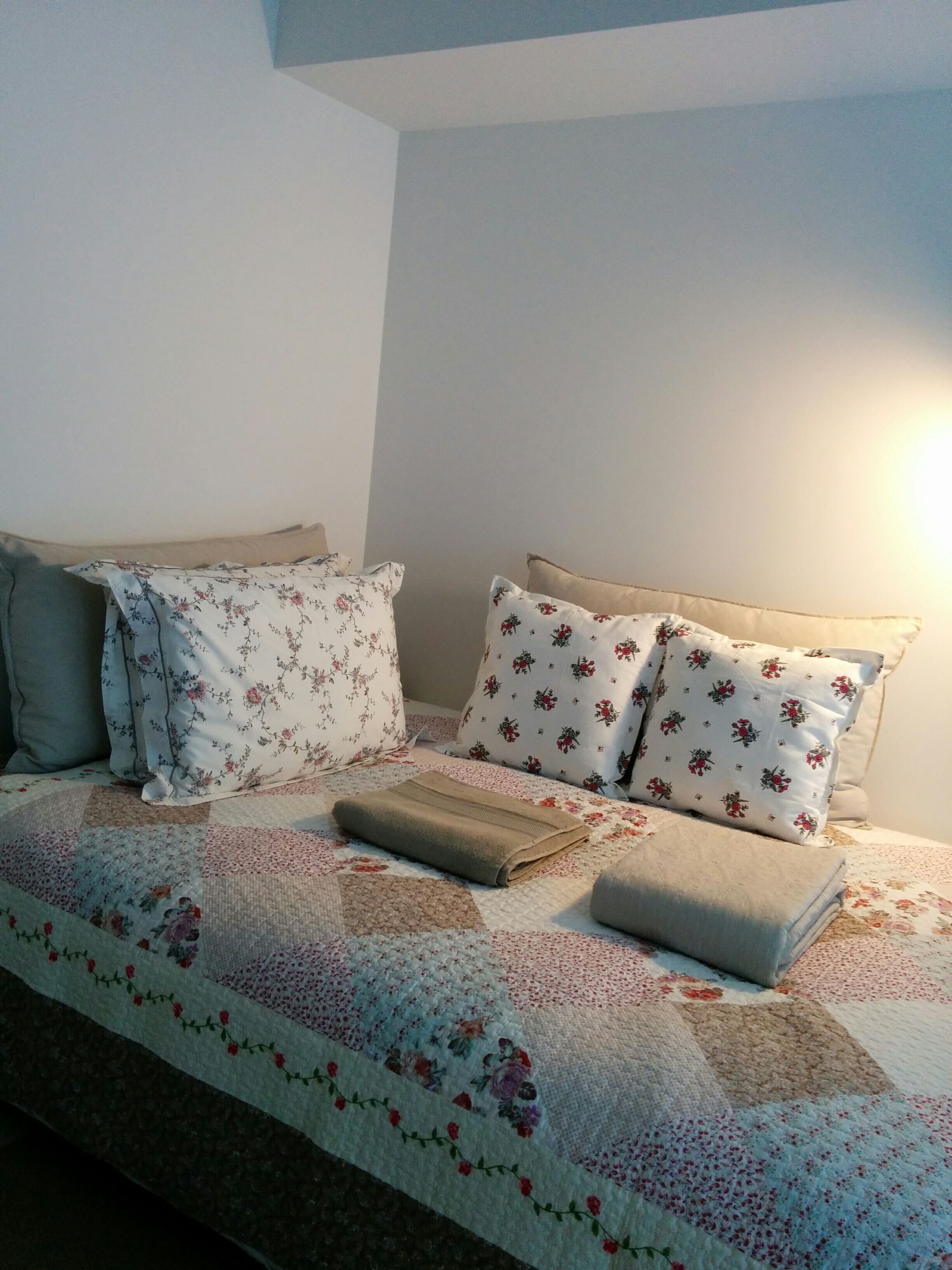 A bed with floral bedding and two pillows, a folded blanket, and a wall with a light source.