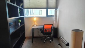 Een ruime, goed verlichte kamer met een bureau, stoel, boekenkast en radiator.