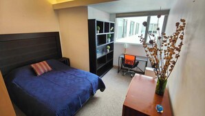 Een slaapkamer met een bed, bureau, stoel, boekenkast en een raam.