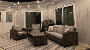 Un espace extérieur aménagé, abrité et doté de mobilier en osier, d’un barbecue et d’une grande porte-fenêtre coulissante.