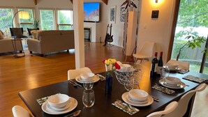 Un coin repas avec une table en bois foncé, dressée pour quatre personnes, des chaises blanches et un vase rempli de fleurs.