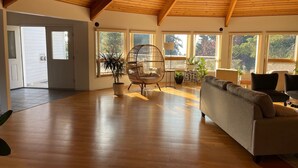Un salon spacieux doté d’un plancher en bois, d’un plafond haut et de grandes fenêtres offrant une vue sur l’extérieur.