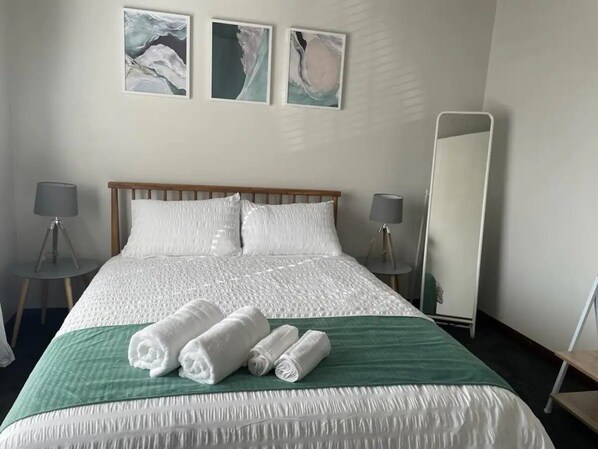 Una habitación de hotel con una cama grande, dos lámparas de noche, un espejo de cuerpo entero y obras de arte en la pared.
