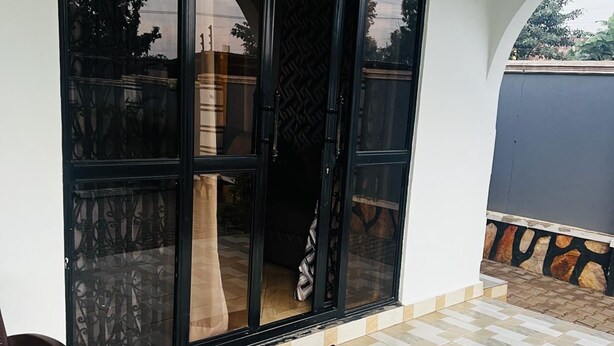 A room with a large sliding glass door, a welcome mat, and a tiled floor. - House - Sleeps 6 - Parking - Garden (Kampala)