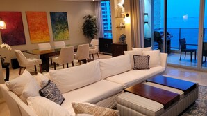 Un salon moderne comprenant un canapé, une table basse et un coin repas. Il y a un balcon avec vue sur l’océan.