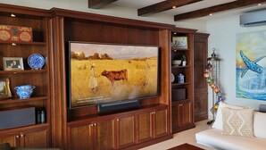 Un salon avec un grand téléviseur à écran plat fixé à un meuble en bois, un canapé blanc et un tableau représentant une baleine accroché au mur.