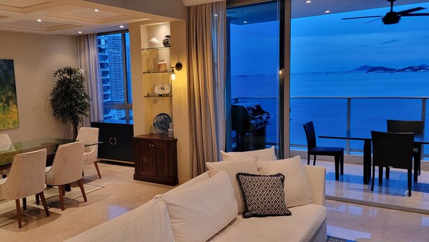 Un salon moderne avec une table à manger en verre, des canapés blancs et une vue sur la mer.