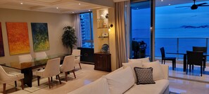 Un salon moderne avec une table à manger en verre, des canapés blancs et une vue sur la mer.