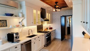 Une cuisine moderne avec des meubles blancs, un four encastré, un lave-vaisselle en acier inoxydable et un ventilateur de plafond.