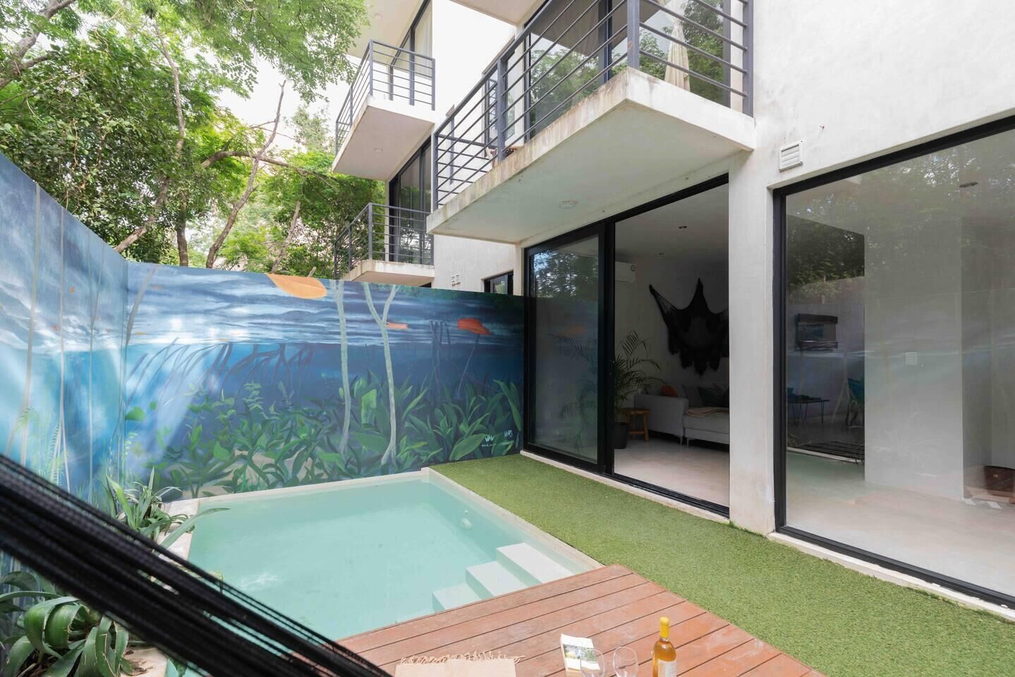 Una casa moderna amb piscina, un balcó i un mural de plantes sota l'aigua.