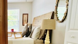 Une chambre à coucher avec un lit, une table de chevet avec une lampe, un miroir et une fenêtre avec des stores.