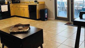 Un vaste espace de vie comprenant une cuisine, une table à manger et une porte-fenêtre coulissante donnant sur une terrasse extérieure.