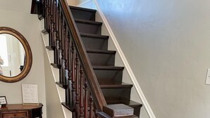 A wooden staircase with dark steps and a handrail, leading to a landing with a welcome sign. - Modern Victorian - 1910 Guesthaus (Hermann)