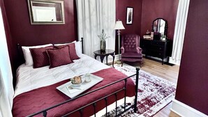 A bedroom with a large bed, a nightstand, a chair, and a dresser. - Modern Victorian - 1910 Guesthaus (Hermann)