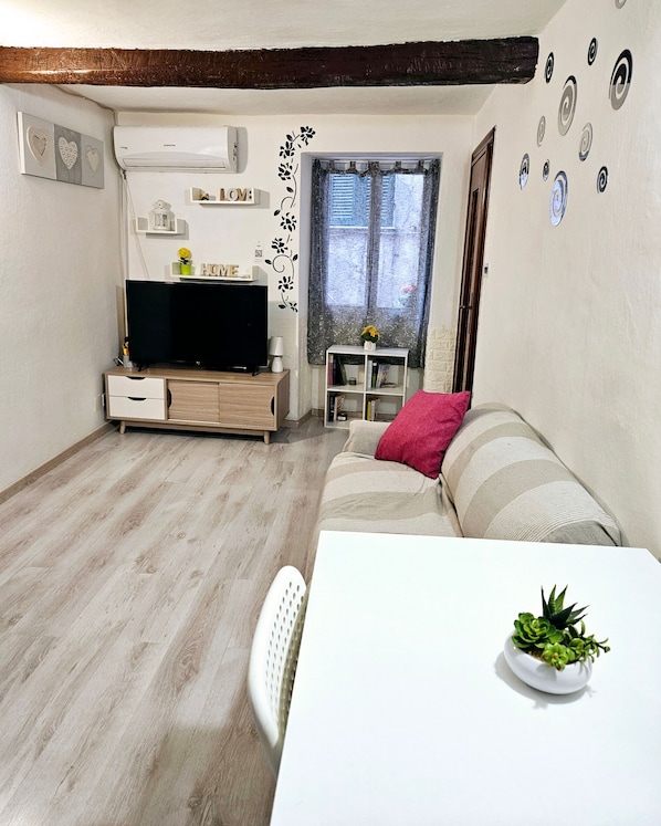 A living room with a flat-screen TV, a sofa, a dining table, and a small plant.