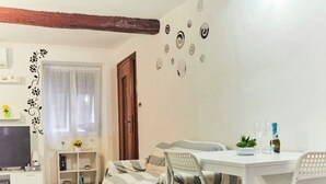 Un salon confortable avec un canapé, une table à manger et des chaises, un téléviseur et une fenêtre avec des rideaux.