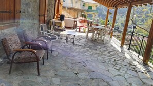 A stone-paved patio with outdoor furniture, including chairs and a table, under a wooden pergola.