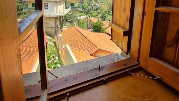 A wooden balcony with a view of a hillside and neighboring houses.