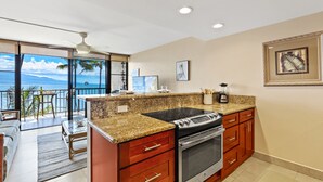 A kitchen with granite countertops, a built-in oven, and a large window overlooking a balcony with a view of the ocean.