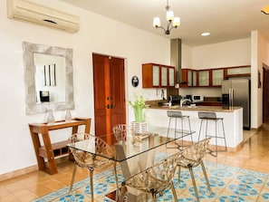 A modern kitchen with a glass dining table, wooden chairs, and a central island.