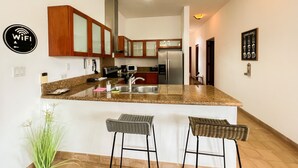 Una cocina moderna con encimeras de granito, electrodomésticos de acero inoxidable y armarios de madera. Hay dos taburetes de bar y una planta en maceta.