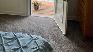 A bedroom with a door leading to a patio. The room has a carpeted floor, a bed, and a wooden dresser. The patio has a table with chairs, a red umbrella, and potted plants. -  Three bedroom home near the University of New Mexico and heart of Albuquerque (Albuquerque)