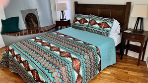 A neatly made bed with a patterned bedspread, a wooden headboard, and a bedside table with a lamp. -  Three bedroom home near the University of New Mexico and heart of Albuquerque (Albuquerque)