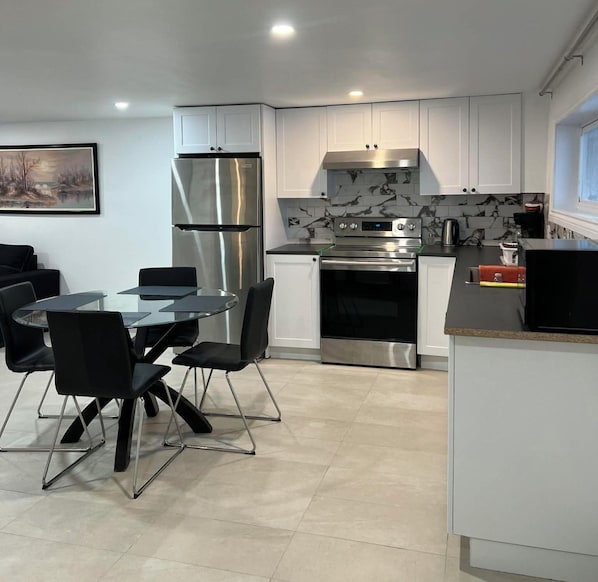 A modern kitchen with a dining area, featuring stainless steel appliances, marble backsplash, and a glass table with chairs.