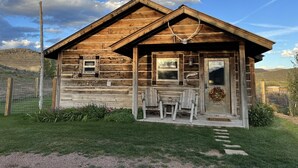 A rustic wooden cabin with a porch, a table, and two chairs.