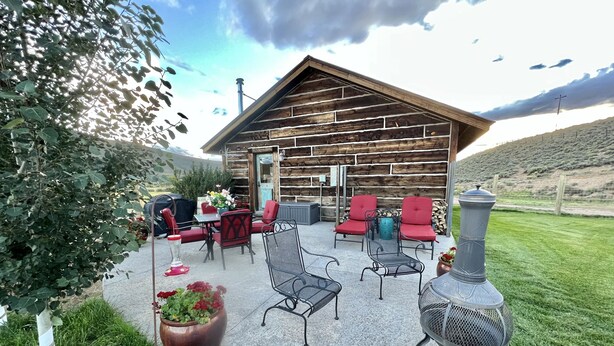 A rustic cabin with a patio area featuring outdoor seating and a wood-burning stove.