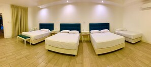 A hotel room with four beds arranged in a U-shape, a wooden floor, and a curtain on the left side. - Hotel Kinova (Salinas)