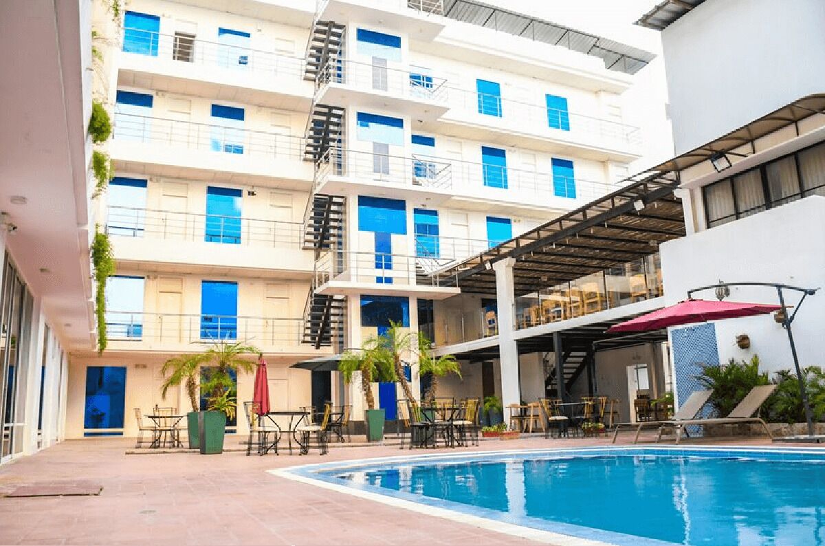 Un hotel con piscina, mobiliario exterior y un edificio de varios pisos con balcones.
