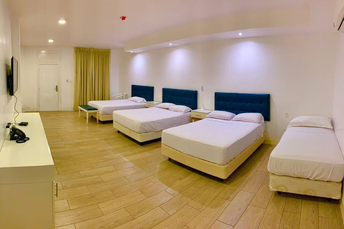 A hotel room with four beds, a desk with a computer, and a TV mounted on the wall.