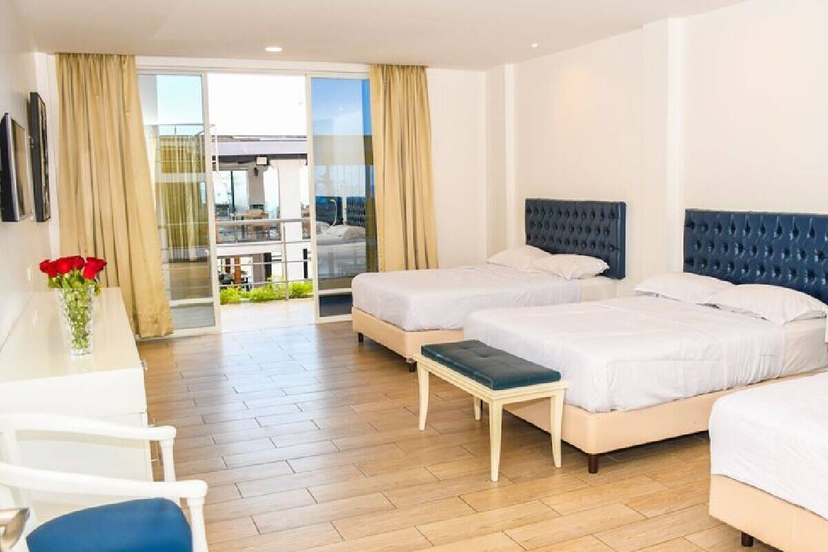 A hotel room with two beds, a desk, a chair, and a view of a balcony.