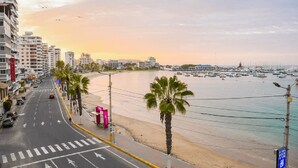Una calle costera con playa, palmeras y un puerto deportivo.