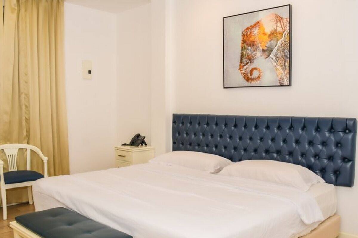 A bedroom with a large bed, a headboard, a bedside table, a chair, and a painting on the wall.