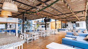 Un amplio espacio lounge al aire libre con suelo de madera, mobiliario blanco y una zona de bar.