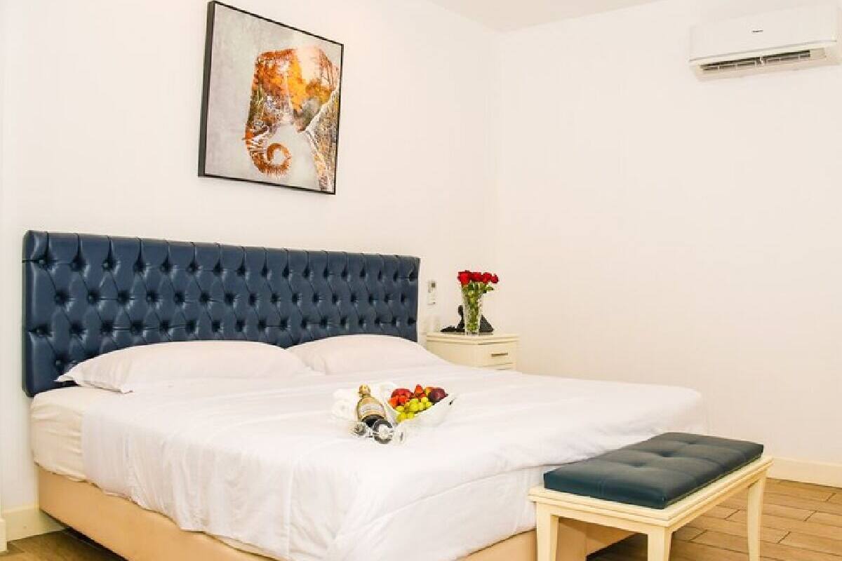 A bedroom with a large bed, a bedside table with a vase of flowers, and a wall-mounted air conditioner.