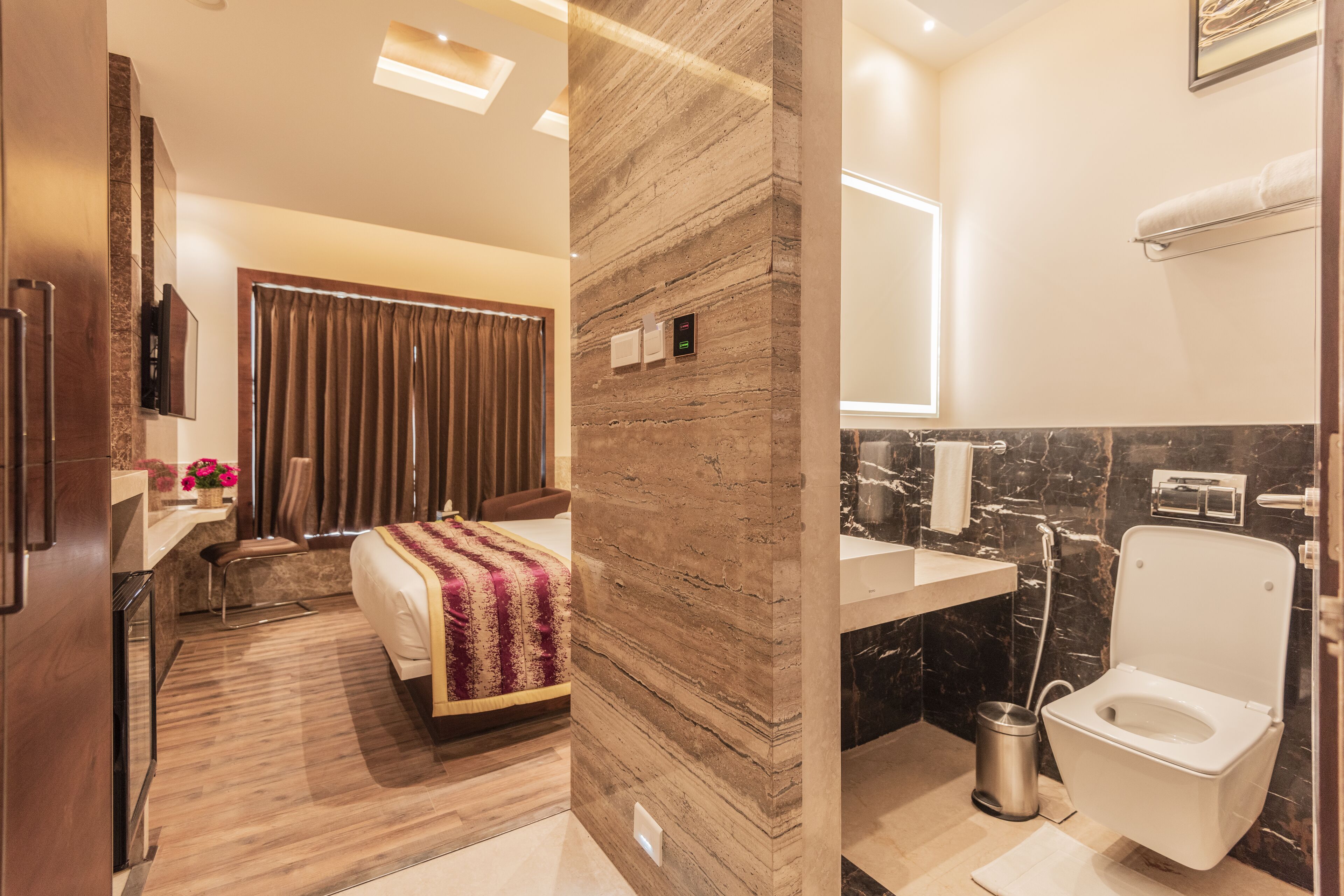 Una habitación de hotel moderna con cama, escritorio, baño con inodoro y lavamanos, y una pared de mármol.
