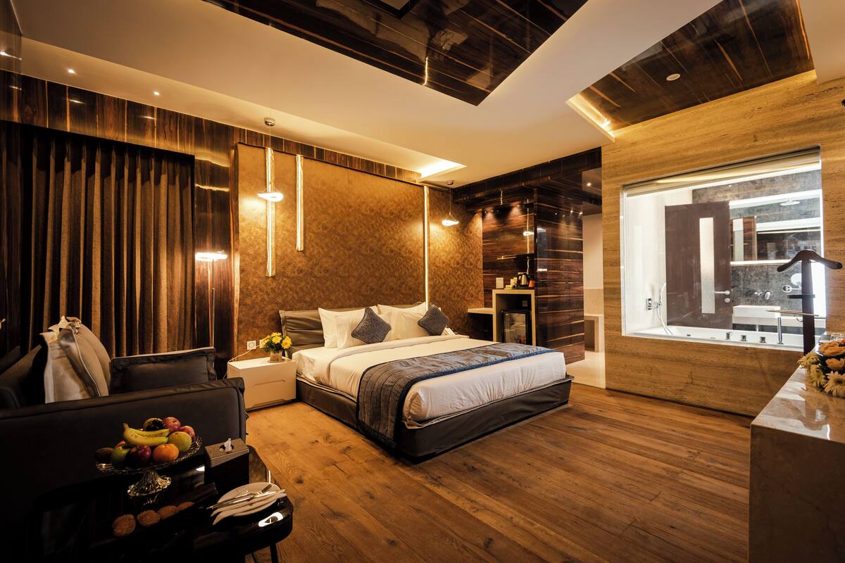 Een moderne slaapkamer met een groot bed, houten vloeren, een bureau met een fruitschaal en uitzicht op buiten.