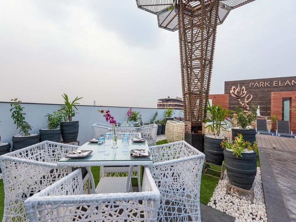 A rooftop patio with white wicker furniture, potted plants, and a view of a building with 'PARK ELAN' signage.