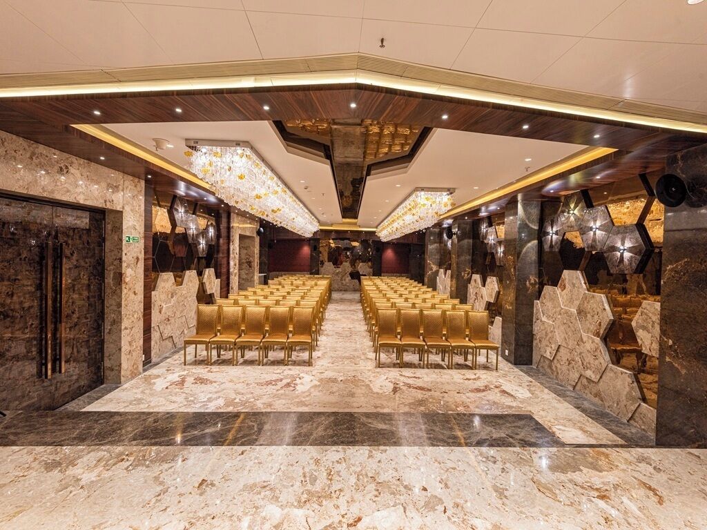Un'ampia sala con file di sedie dorate e pavimento in marmo, caratterizzata da un design moderno del soffitto e dettagli murari in pietra.
