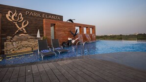 Un edificio moderno llamado 'Park Elanza' con un área de piscina que incluye sillas de descanso y una escultura decorativa.