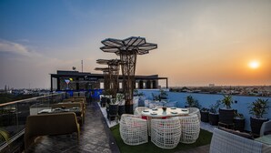 Una terraza en la azotea con mobiliario exterior, una estructura decorativa y vistas del horizonte urbano al atardecer.