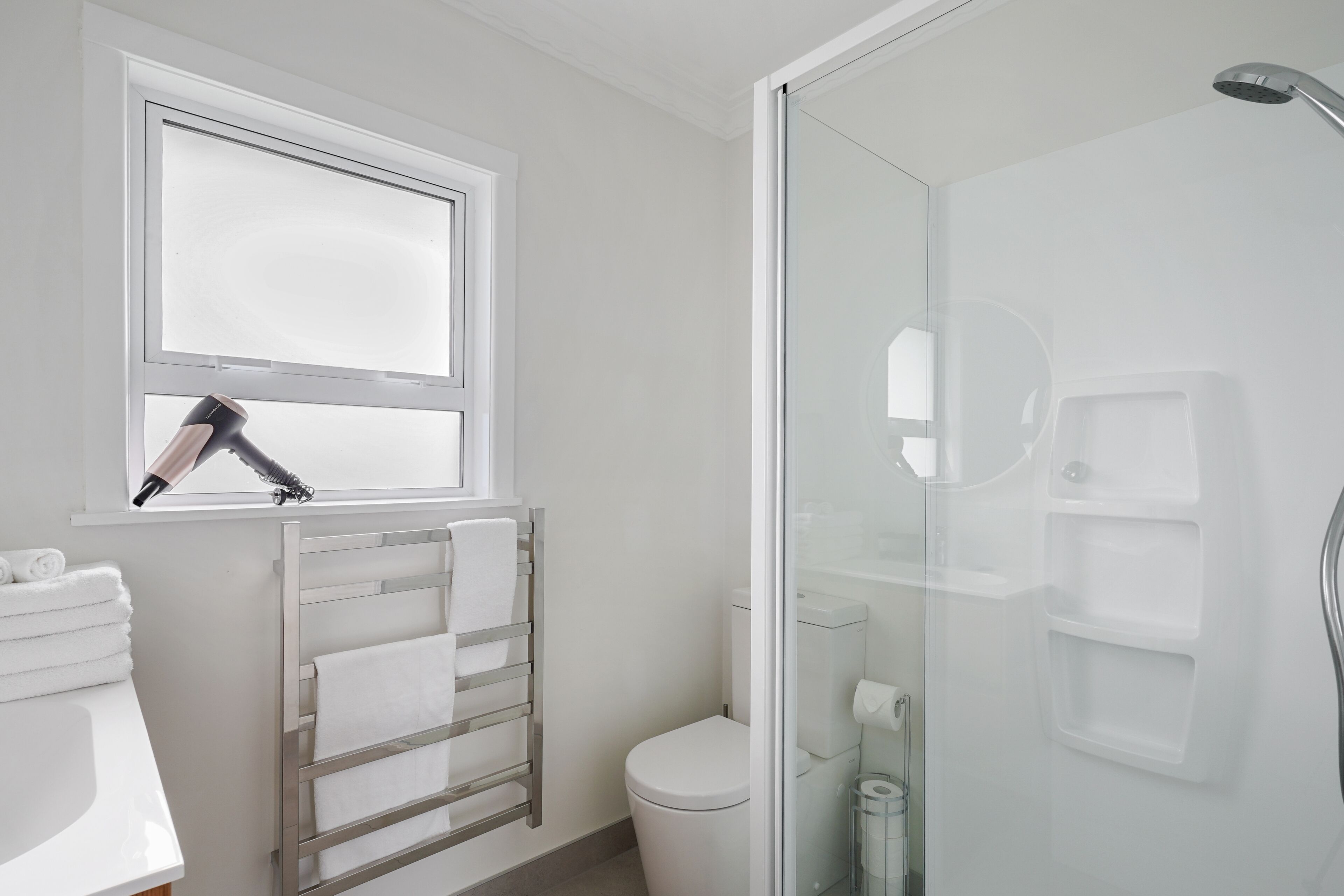 A modern bathroom with a glass shower enclosure, a white toilet, and a towel rack with folded towels.