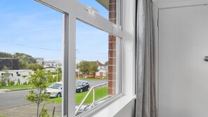 A window with a view of a street, a tree, and a building in the background. - Renovated Takapuna 2BR Apt - Parking (Auckland)